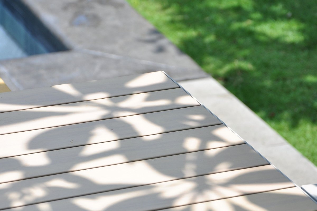 Gray plank deck boards with a leaf shadow pattern and a green lawn beside the deck