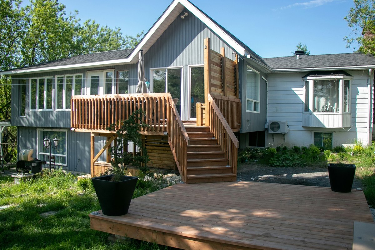 New cedar raised deck with a wide stair down to a ground-level deck behind a gray-sided house