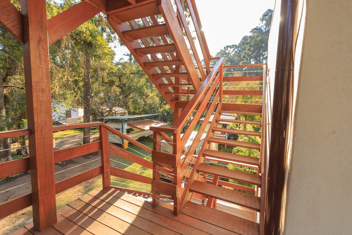 New red-stained wood deck with a two-flight staircase and cable railings beside a cream stucco wall