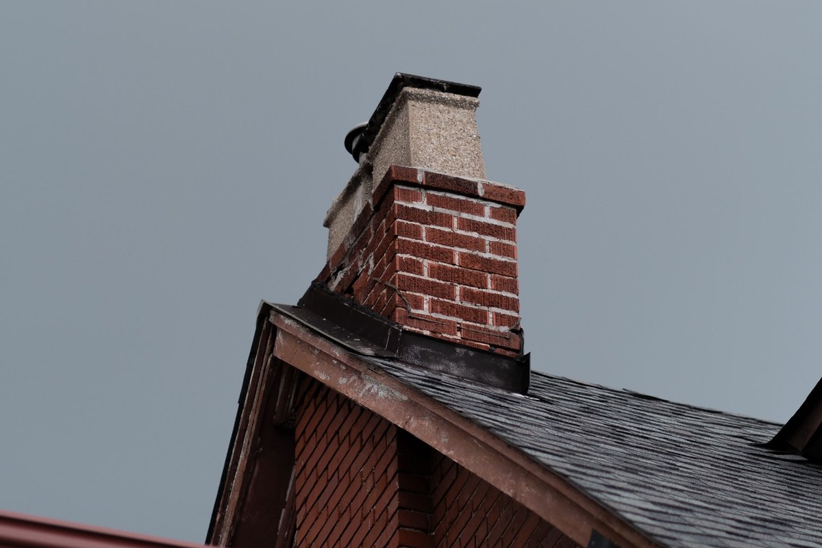 Brick chimney with black flashing where it meets a dark asphalt shingle roof