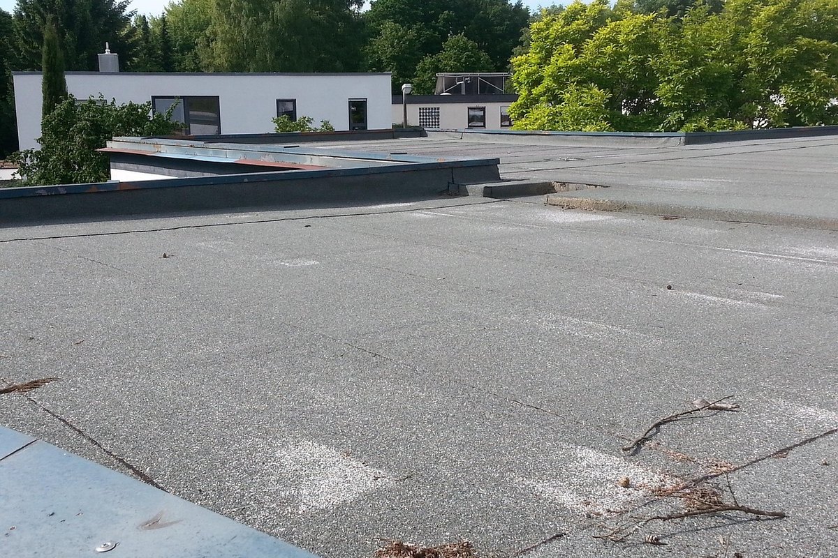 Flat roof covered in gray granulated membrane with metal-capped edges and twigs on the surface