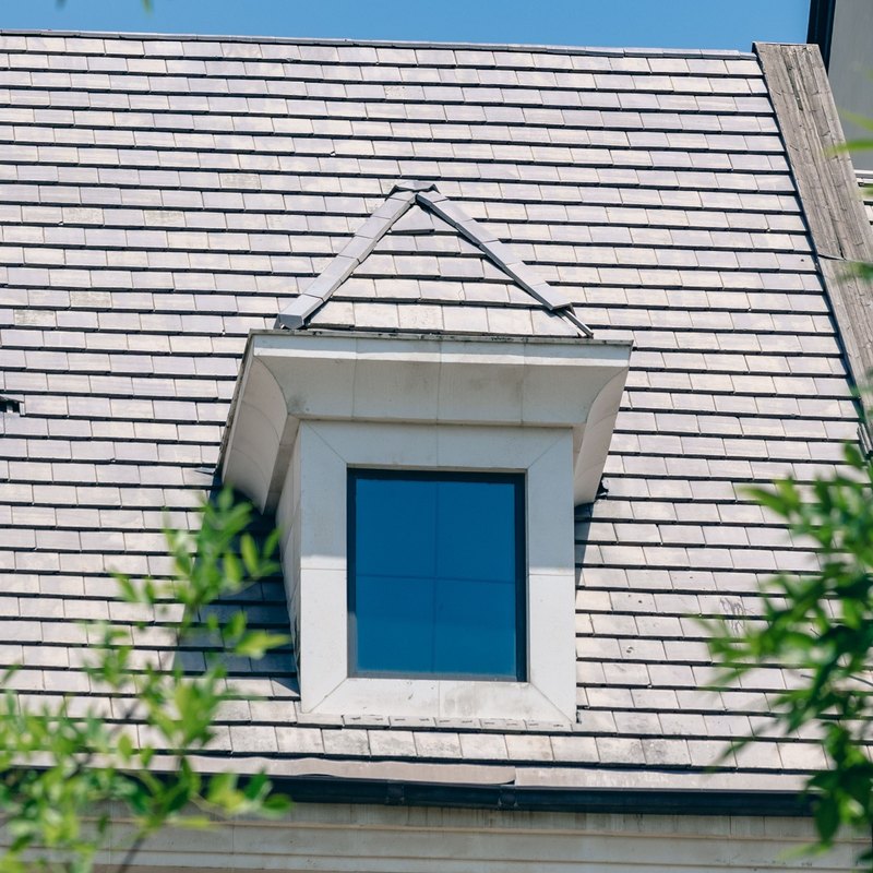 Steep gray roof with neat overlapping rows and a white-trimmed dormer window under a blue sky