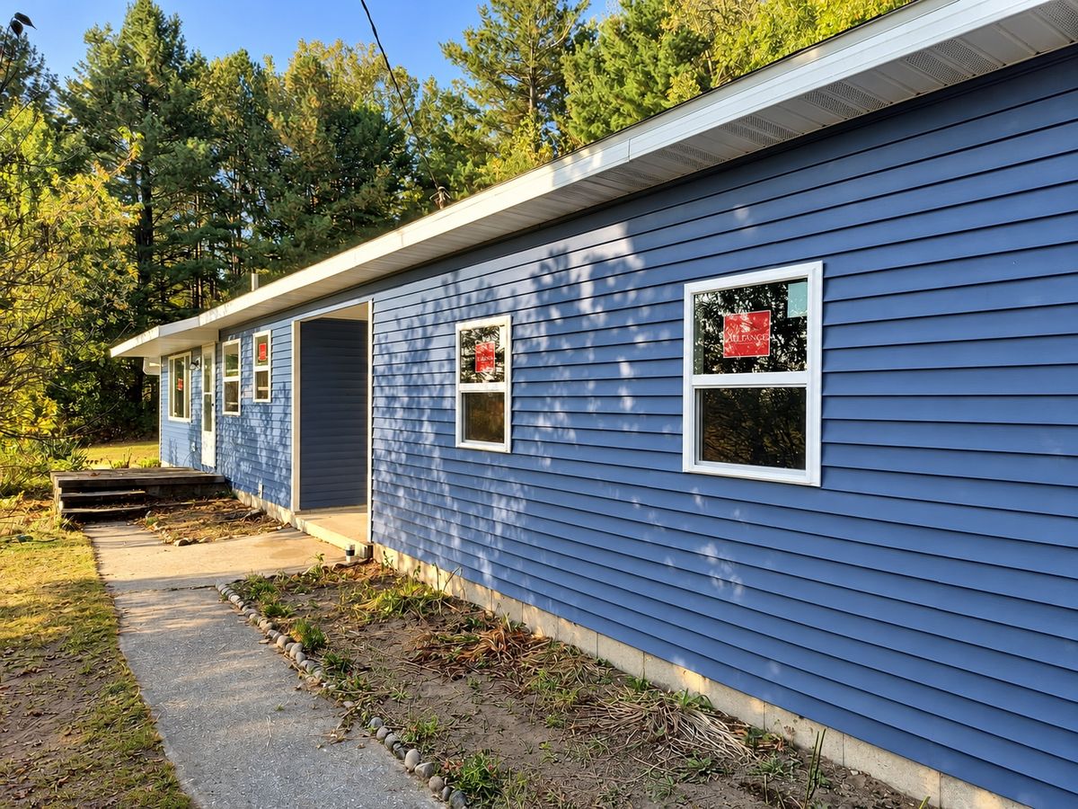 One-story ranch house in periwinkle blue vinyl siding with two new windows and a recessed entry