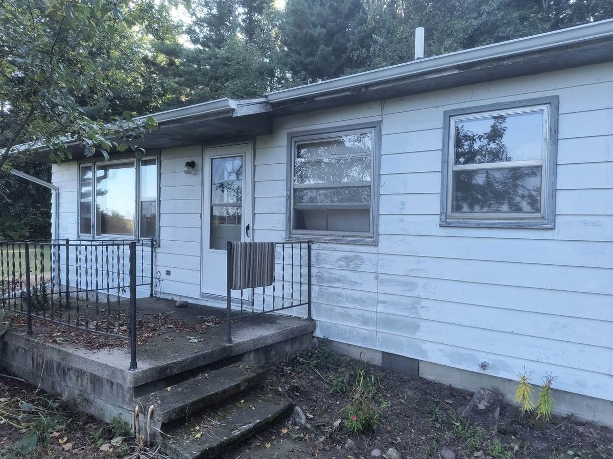 Older house with weathered chalky white lap siding, patched in places, beside a stepped concrete stoop