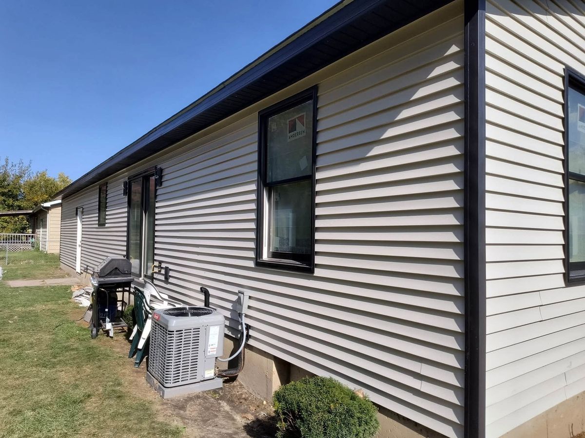 Beige vinyl-sided ranch wall with black-framed new windows and a sliding door