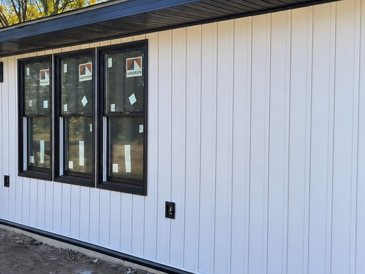 White vertical vinyl siding on a one-story house with three new black-framed windows