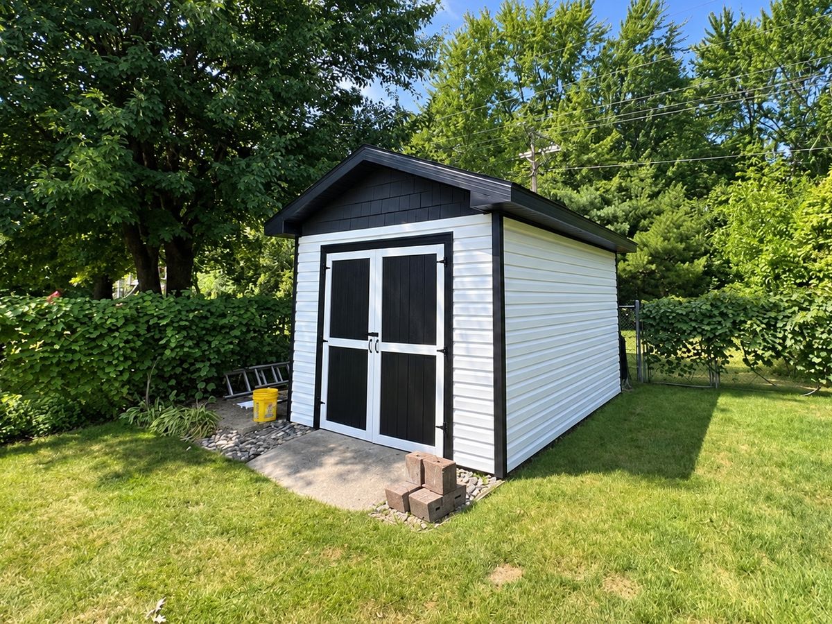 Backyard shed with white horizontal vinyl siding, black trim and black double doors