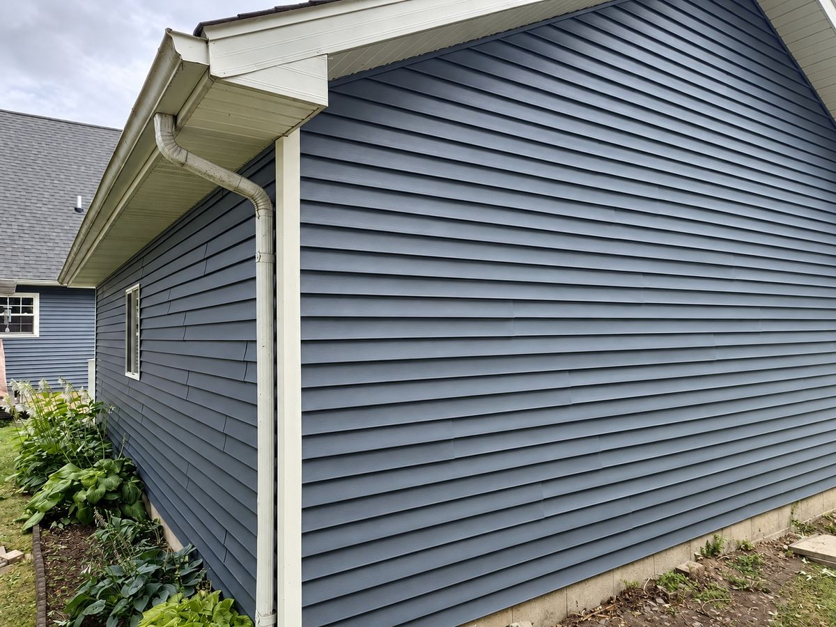 Slate blue-gray horizontal vinyl siding on a house wall with white soffit, gutter and downspout
