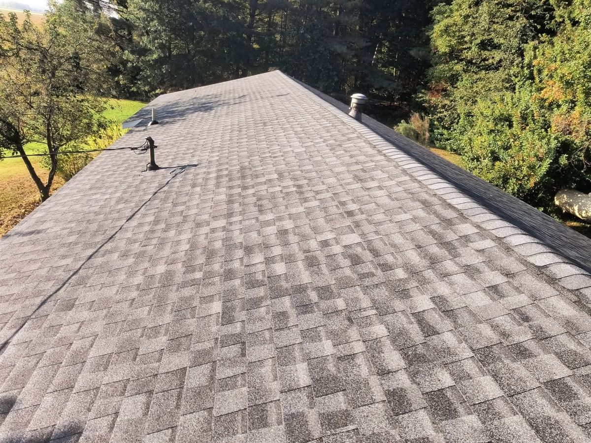 Finished gray-brown asphalt shingle roof seen from above with a capped ridge and roof vents
