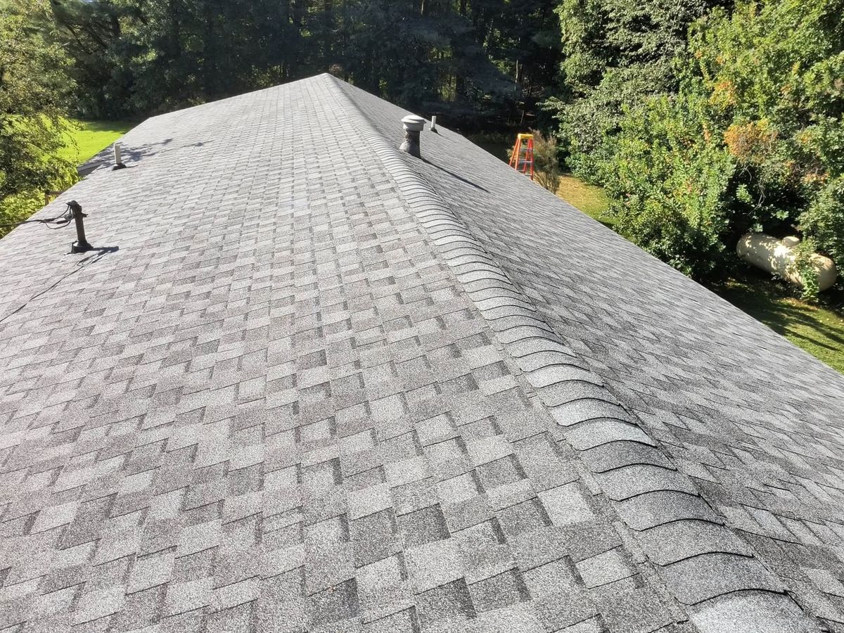 Aerial view up a finished gray asphalt shingle roof with a capped hip running to the right