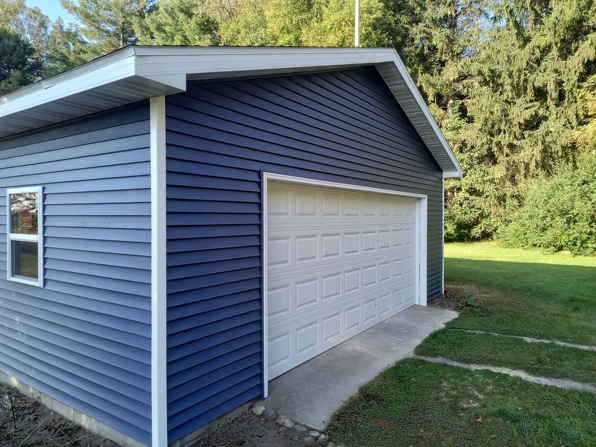 Detached garage with navy blue horizontal vinyl siding, white trim and a white overhead door
