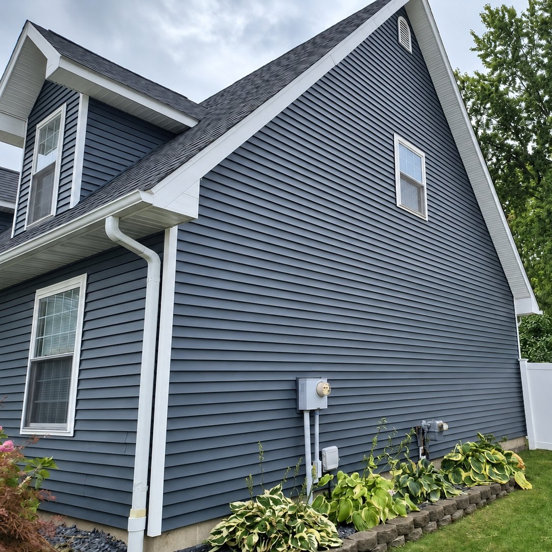 Slate gray vinyl siding on a two-story house gable with a window and white trim