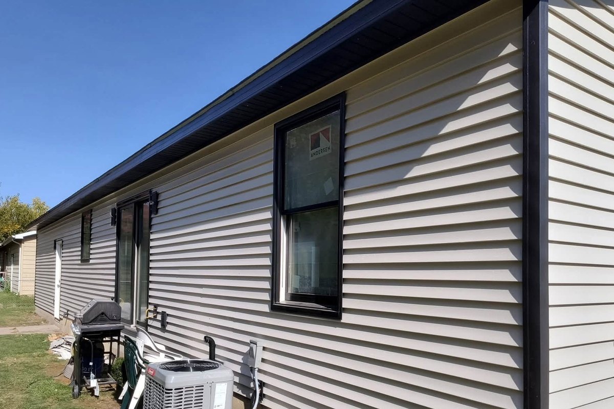 Beige vinyl-sided ranch wall with black-framed new windows and a sliding door