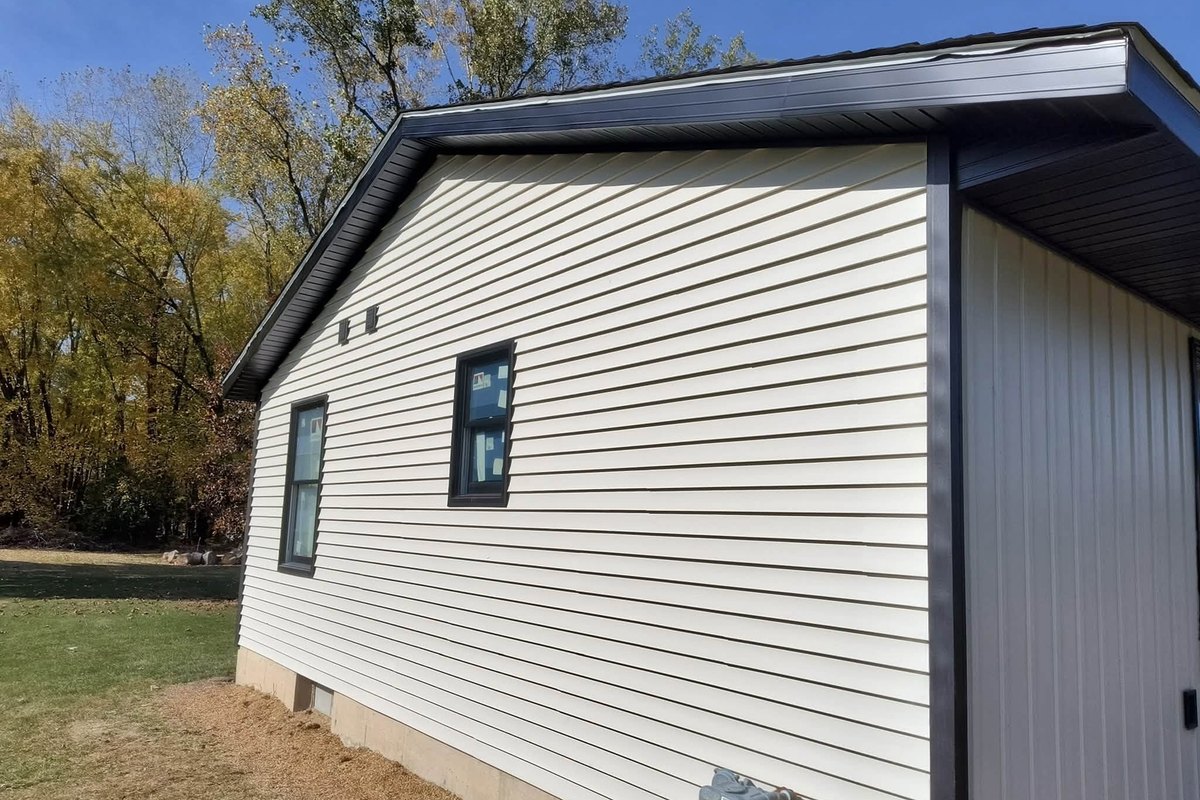 Cream horizontal vinyl siding on a gable wall with two new black-framed windows still in film