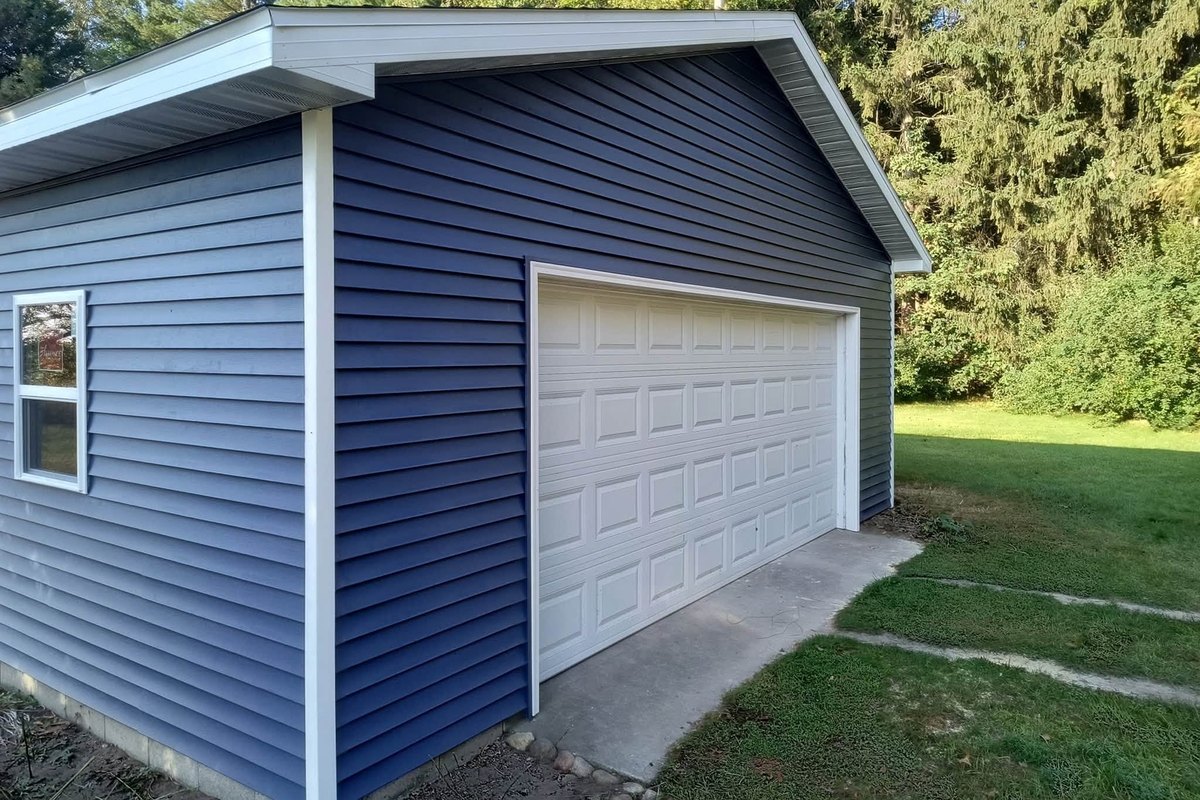 Detached garage with navy blue horizontal vinyl siding, white trim and a white overhead door