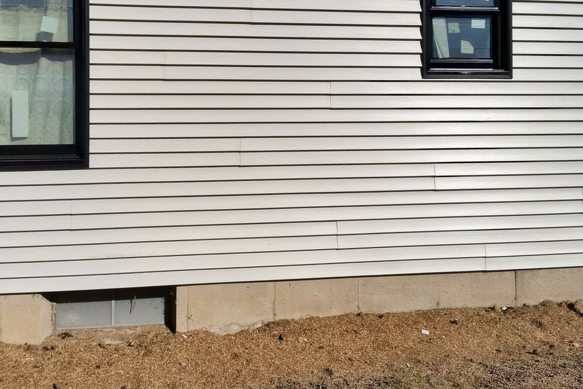 Beige horizontal vinyl siding on a house wall with black-framed new windows