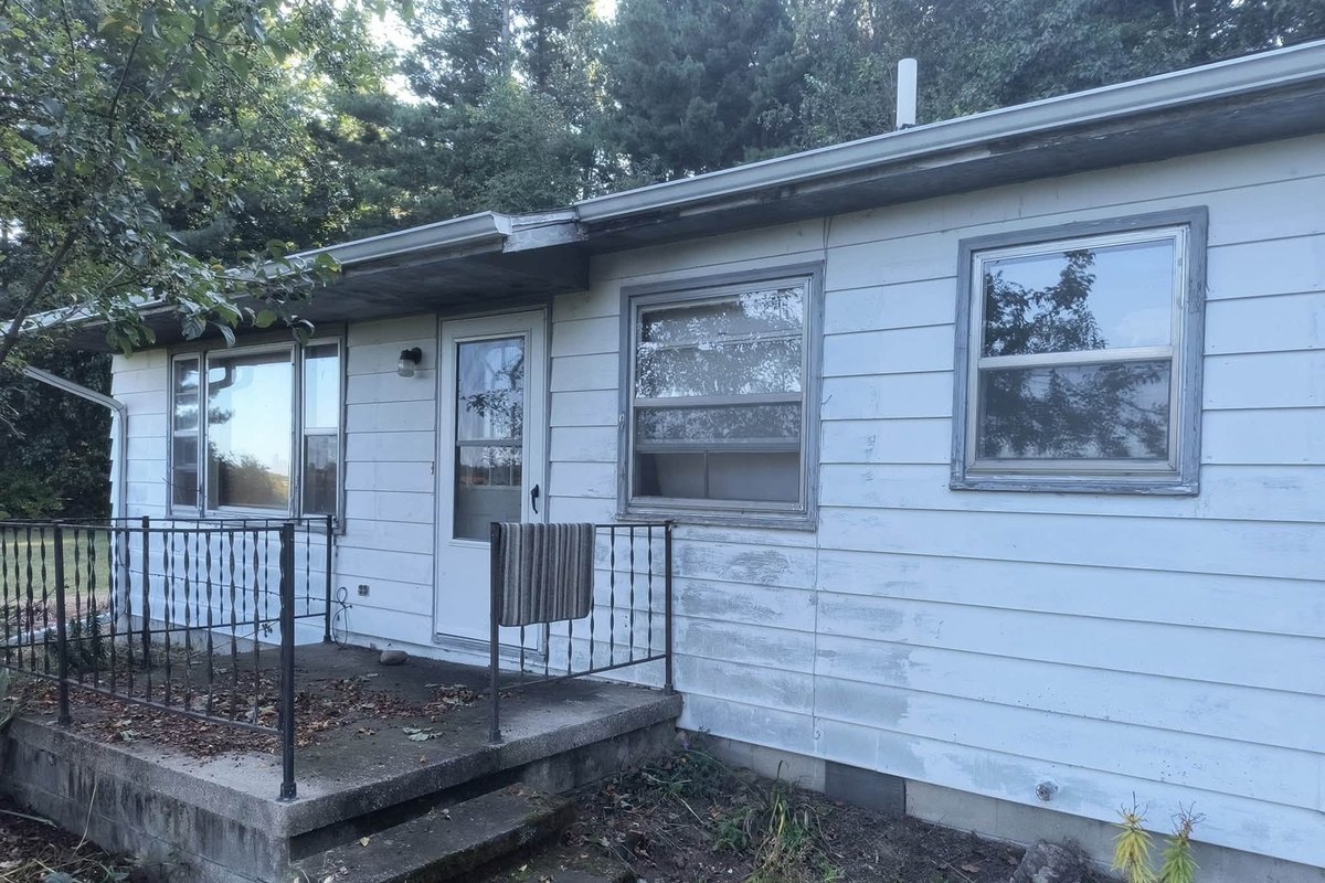 Older house with weathered chalky white lap siding, patched in places, beside a stepped concrete stoop