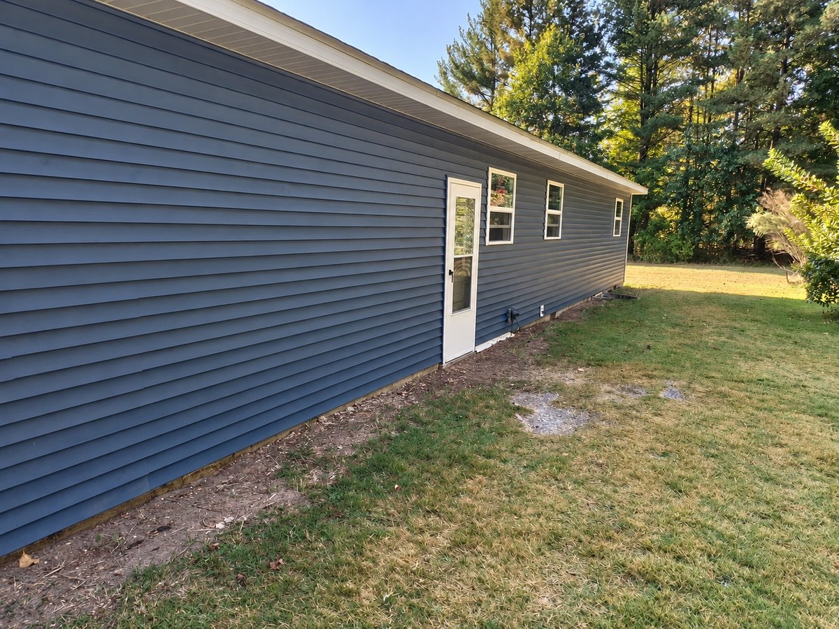 The same long low house after re-siding, with slate-blue vinyl siding, white trim and new windows