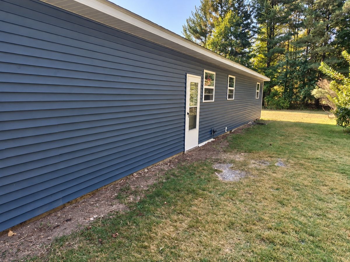 Long side wall of a one-story house in dark slate blue vinyl siding with a white entry door and small windows