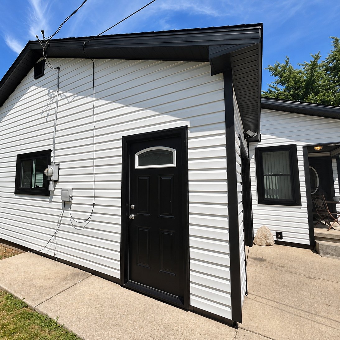 Small house corner in white horizontal vinyl siding with black trim and a black entry door