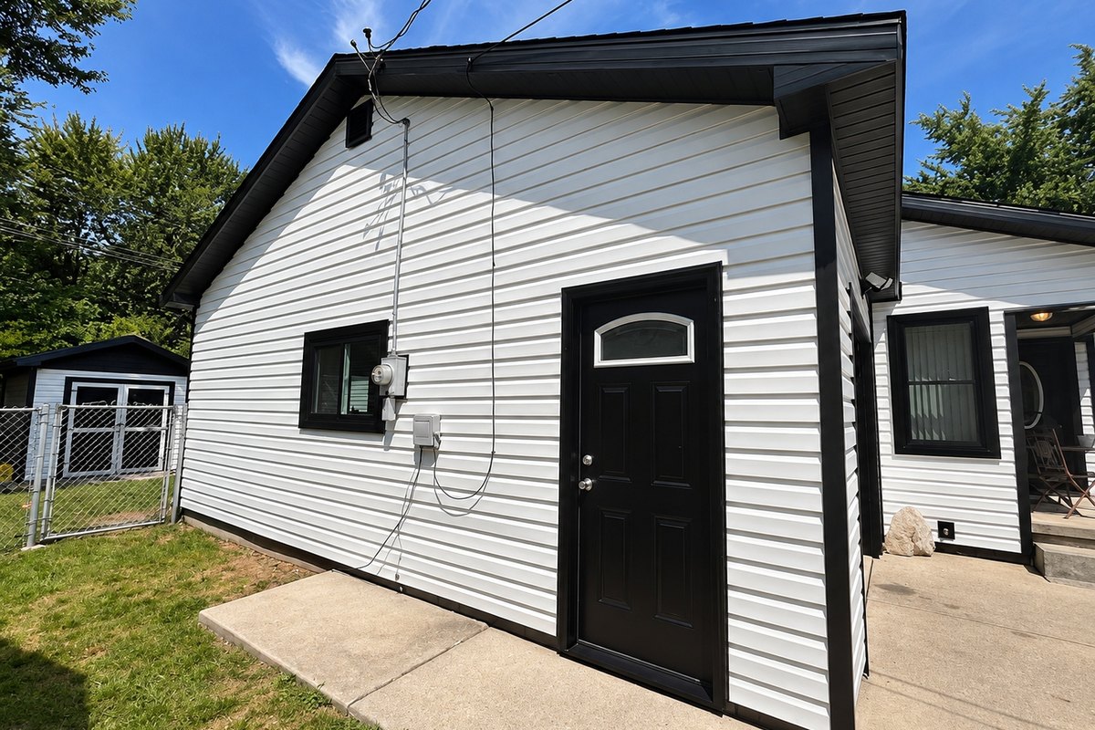 Small house corner in white horizontal vinyl siding with black trim and a black entry door