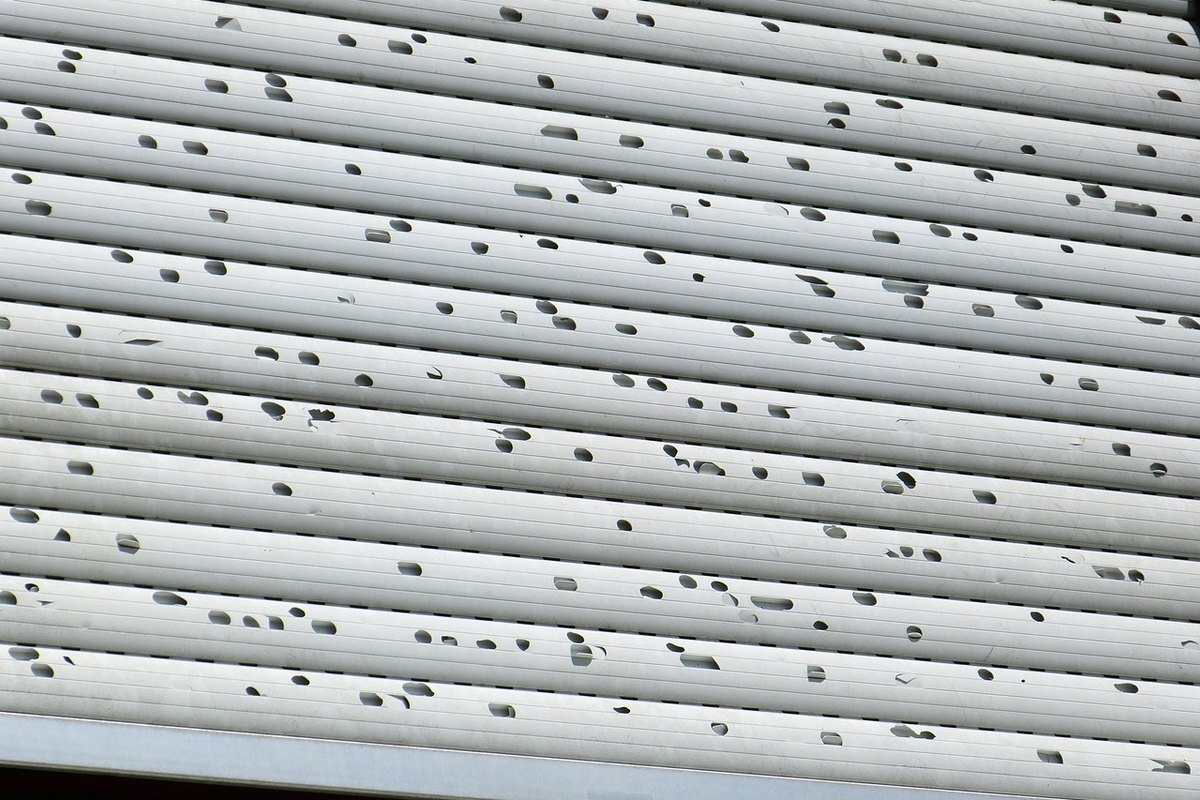 Window shutter slats punched full of dents and holes by hail