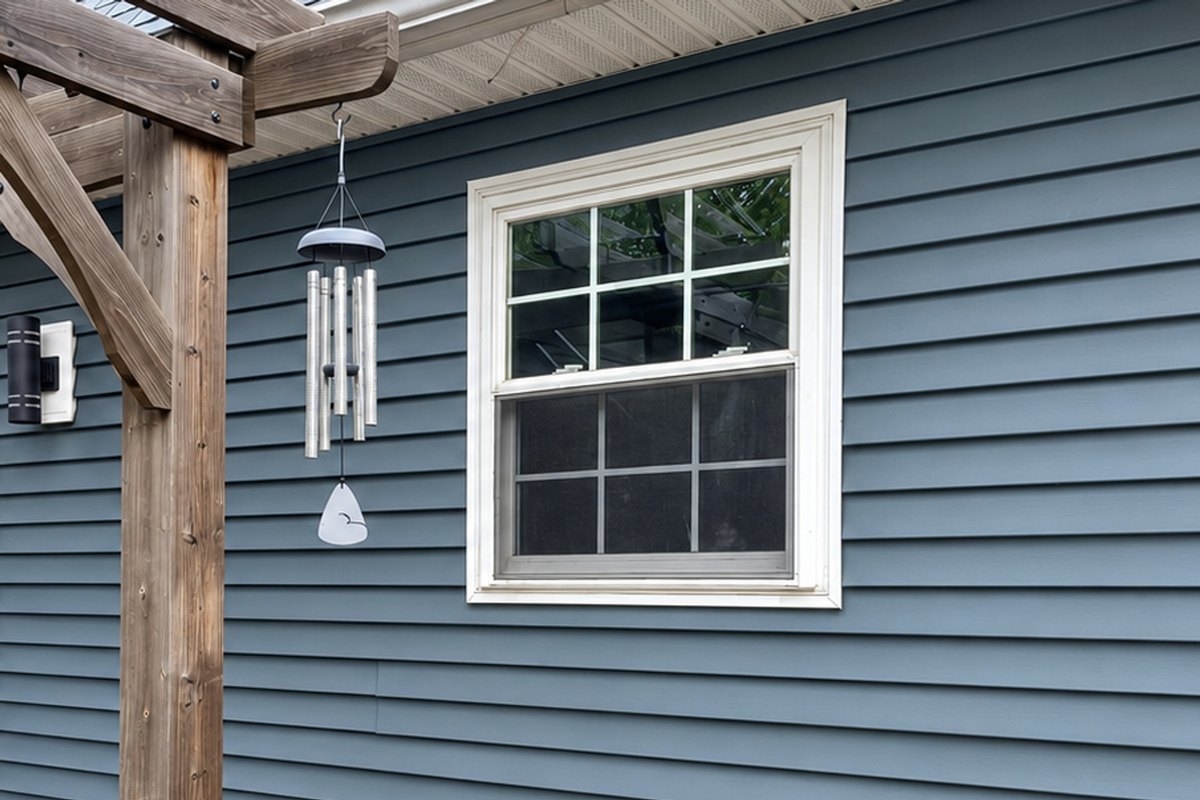 Rear wall of a house in slate blue-gray vinyl siding with a wood pergola over a brown deck and a double-hung window